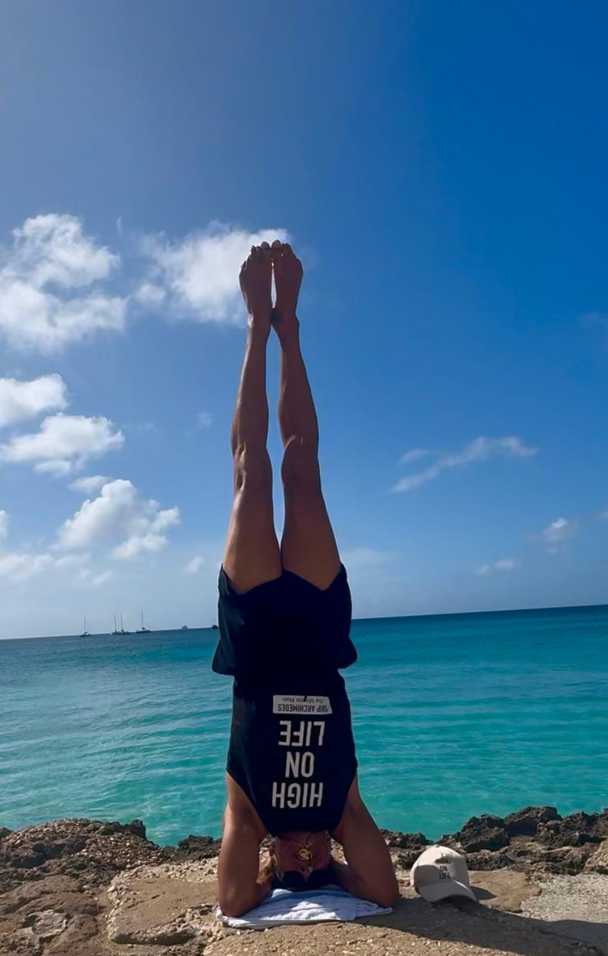 Skip Archimedes in a headstand on a beach, wearing a 'High on Life' t-shirt